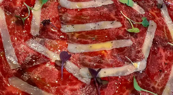 Finas lonchas de jamón ibérico, un manjar de moda, con un toque de pimienta y brotes verdes.