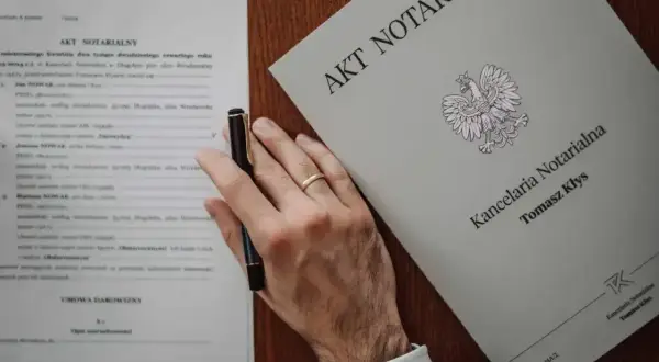Dłoń z piórem nad dokumentem "Akt notarialny", obok księga "Kancelaria Notarialna Tomasz Kłys".