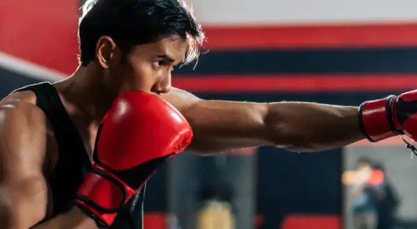 Boxer throws a powerful punch, aiming for the sternum. Red gloves flash as he trains in the ring.