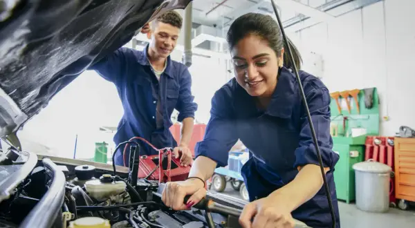 Deux mécaniciens en bleu travaillent sur un moteur de voiture, effectuant un pré contrôle technique.