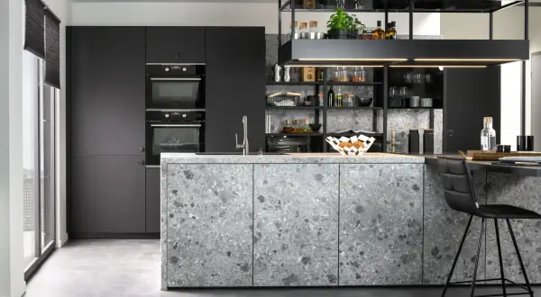 Cuisine moderne aux façades grises et à l'îlot central en sol terrazzo. Électroménagers intégrés et étagères noires remplies d'objets décoratifs.