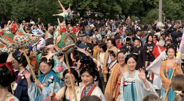 Bunte Drachenköpfe und Menschen in traditionellen Gewändern beleben den **Carnival Berlin**. Eine fröhliche Parade zieht durch die Menge.