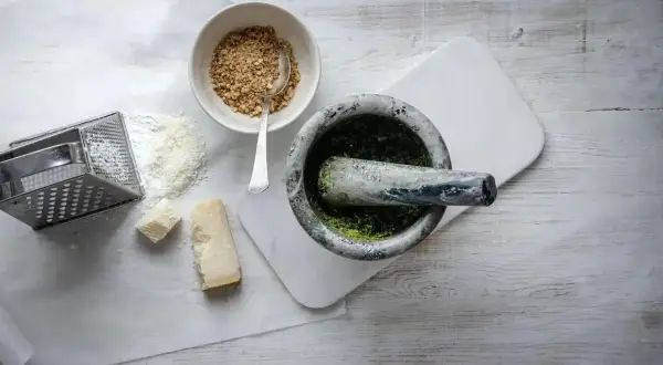 Mortel med grön pesto, riven parmesan, nötter och rivjärn. Ingredienser för ett klassiskt pesto recept.