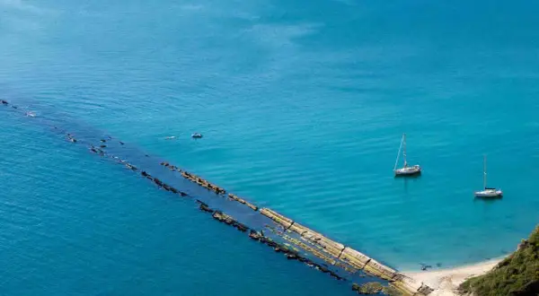 La spiaggia del Trave, con le sue acque turchesi, ospita due barche a vela e un piccolo motoscafo.