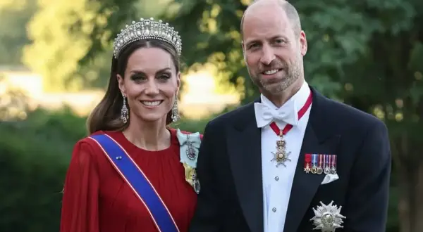 Kate i William w królewskich strojach, z diademem i medalami, uśmiechają się do zdjęcia.