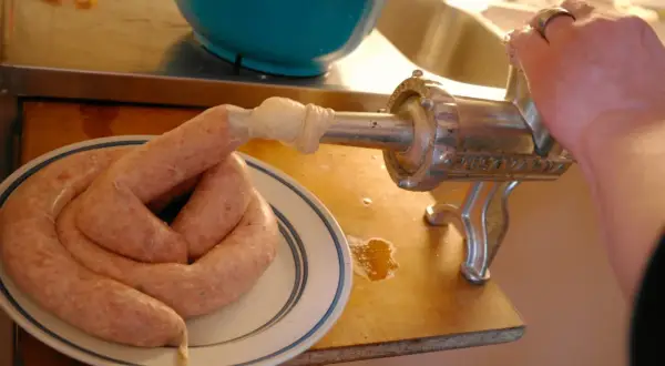 En hand vrider på en köttkvarn som gör korv. Ett korv-recept blir verklighet på tallriken.