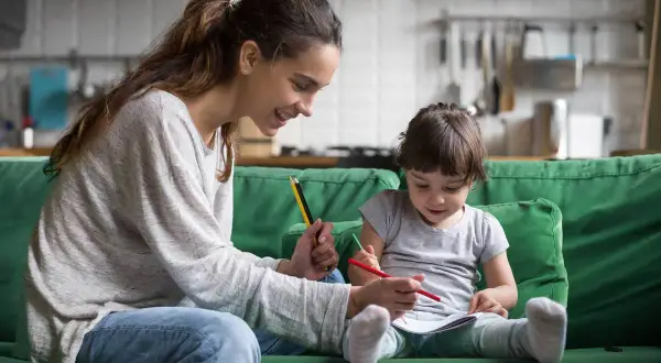 Uśmiechnięta mama pomaga dziecku w rysowaniu. Wspólna praca dla dzieci, rozwijająca kreatywność i więź.
