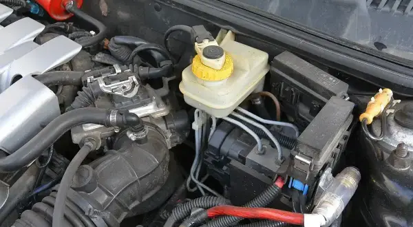 Silnik samochodu z widocznym zbiorniczkiem płynu hamulcowego i elementami układu elektrycznego. To właśnie serwo pomaga w hamowaniu.