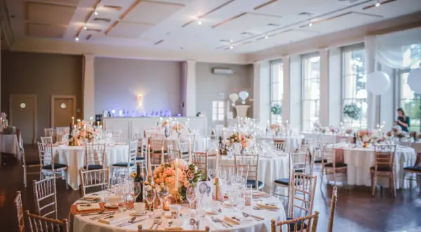 Elegancka sala imprez okolicznościowych przygotowana na przyjęcie. Okrągłe stoły nakryte białymi obrusami, ozdobione kwiatami i świecami.
