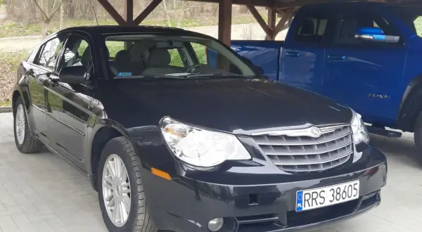 Czarny Chrysler Sebring pod wiatą, obok niebieski pickup.