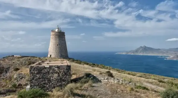 El faro de Almería se alza sobre una colina rocosa, vigilando el mar azul bajo un cielo nublado.