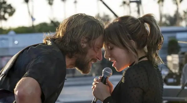 Bradley Cooper i Lady Gaga śpiewają razem, zbliżając twarze do mikrofonu.