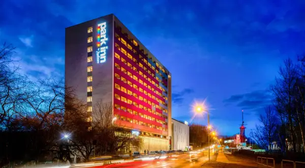 Wieczorna panorama miasta z oświetlonym budynkiem Park Inn Hotel Katowice i smugami świateł samochodów na drodze.