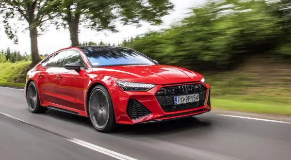 Czerwone Audi RS 7 pędzi po drodze, otoczone zielenią drzew.