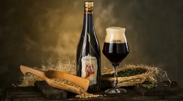 Una bottiglia e un bicchiere di birra Zahre, con chicchi d'orzo e luppolo, ingredienti per una birra artigianale di qualità.
