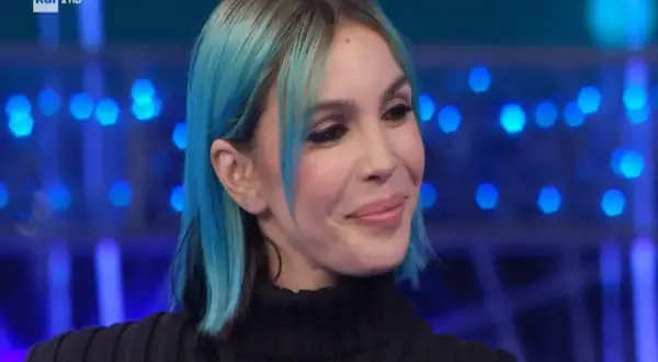 Una donna con capelli blu e neri, trucco marcato, sorride con un'espressione da rose villain.