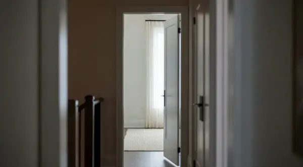 Korytarz z otwartymi drzwiami prowadzącymi do jasnego pokoju z zasłonami. Widoczny fragment balustrady schodów. 193 kk.