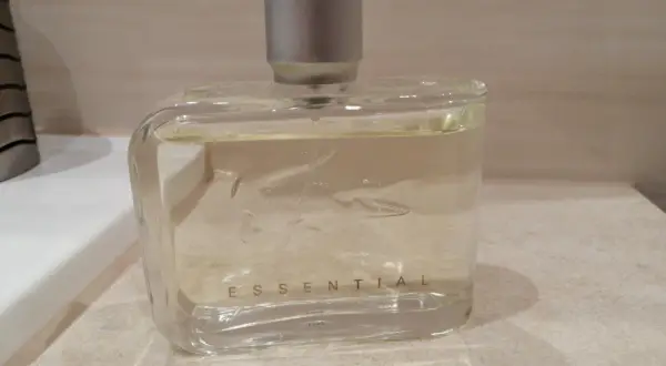 Szklana butelka perfum Lacoste Essential Sport z srebrną nakrętką, stojąca na blacie.