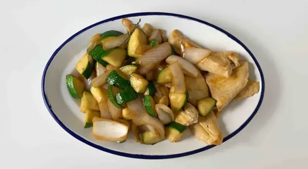 Sabroso pollo con calabacín y cebolla salteados, servido en un plato blanco con borde azul.