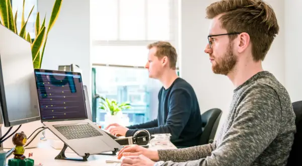 Deux développeurs travaillent sur leurs ordinateurs portables, plongés dans le code. Une scène typique d'une école de développeur moderne.