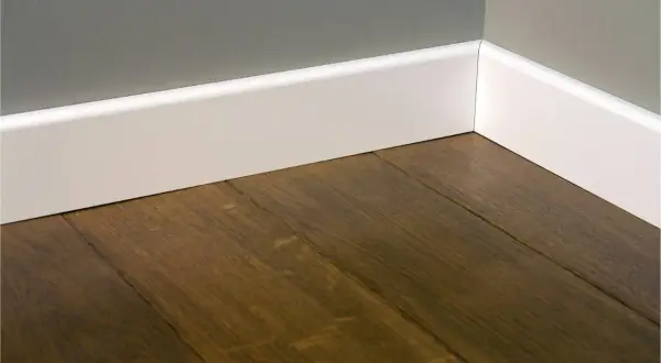 Esquina de una habitación con suelo de madera oscura y rodapiés blancos lisos, mostrando diferentes tipos de rodapiés.