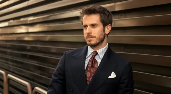 Uomo con abito blu, camicia a righe e cravatta verde con fantasia. Sguardo pensieroso.