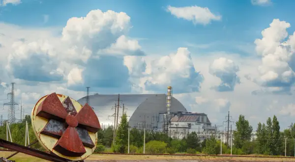Rdzawe koło symbolizujące zagrożenie promieniotwórczością na tle sarkofagu Czarnobylskiej Elektrowni. Kiedy Czarnobyl będzie bezpieczny?