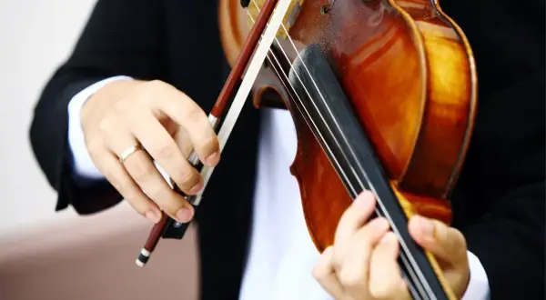 Hände üben das Bratsche lernen. Ein Musiker in schwarzem Sakko hält den Bogen und greift die Saiten der warmbraunen Bratsche.