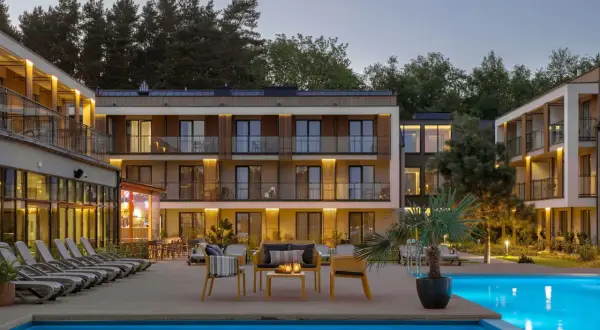 Nowoczesny hotel z basenem i leżakami, otoczony drzewami.