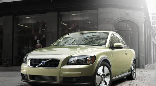 Złoty Volvo C30 segment c zaparkowany na brukowanej ulicy przed sklepem z modą.