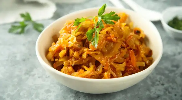 Pyszny bigos z białej kapusty, duszony z marchewką i przyprawami, udekorowany natką pietruszki.