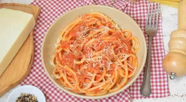 Pyszne bucatini amatriciana z pomidorowym sosem i parmezanem, obok kawałek sera i pieprz.