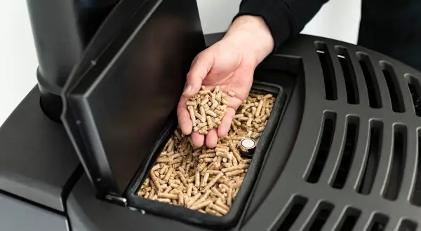 Main d'homme versant des granulés de bois dans un poêle, respectant la norme tubage poele a granulé pour un chauffage efficace et sécurisé.
