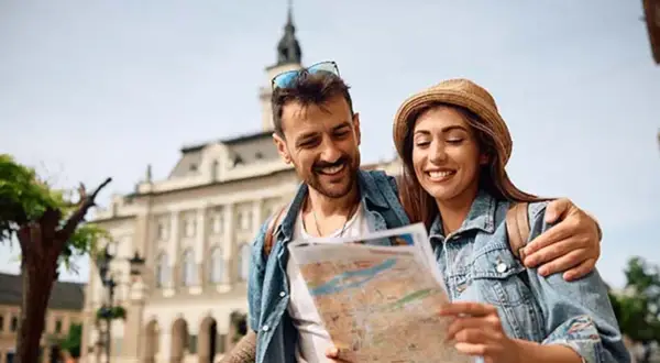 Uśmiechnięta para planuje wyjazd na weekend, studiując mapę na tle zabytkowej architektury.