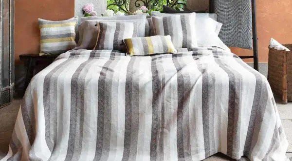 Letto con biancheria a righe grigie e bianche, cuscini coordinati. Un'immagine che ispira su come lavare il lino per mantenerlo morbido.