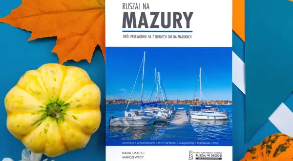 Przewodnik "Ruszaj na Mazury" z widokiem na żaglówki i urokliwe jeziora mazurskie. Jesienne dekoracje dodają uroku.