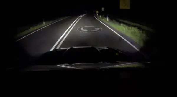 La route de nuit, éclairée par les feux de route, révèle un rond-point.