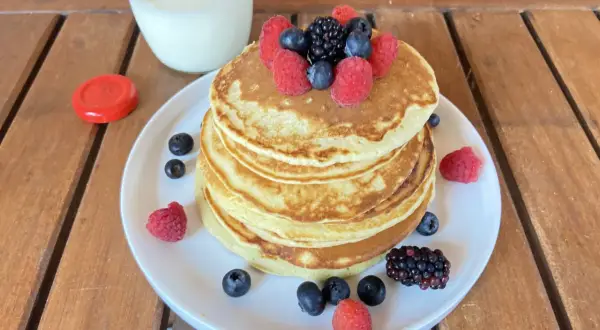 Pancake light con frutti di bosco e un bicchiere di latte su un tavolo di legno.