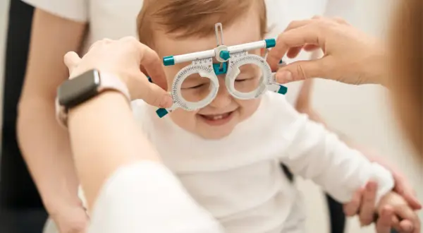 Uśmiechnięte niemowlę z oprawką optometryczną na nosie, jak widzi miesięczne dziecko.