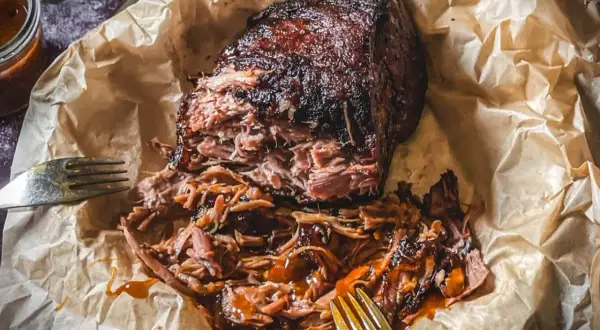 Saftiges pulled pork, zart zerfallen, mit BBQ-Sauce übergossen, auf Backpapier mit Gabeln.