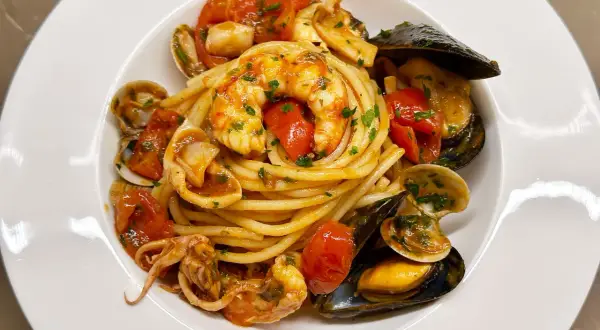 Un piatto invitante di spaghetti allo scoglio, con gamberi, cozze, vongole e calamari, condito con pomodorini e prezzemolo.