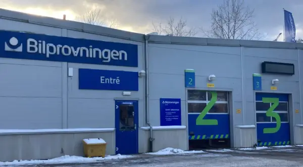 Bilprovningen med entré och garageportar för besiktning. En varningstriangel syns inte, men bilen är redo för kontroll.
