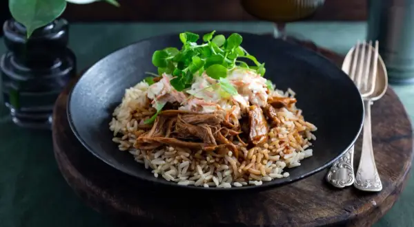 En tallrik med pulled pork med ris, toppad med krispig coleslaw och gröna blad. En härlig måltid som ser utsökt ut.