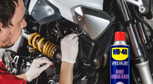 Hombre con guantes blancos trabajando en la cadena de moto. Lata de WD-40 Specialist Bike Degreaser para quitar oxido cadena moto.