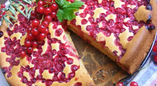Pyszne ciasto z porzeczkami, ozdobione świeżymi owocami i gałązką zboża. Idealne na letnie popołudnie.