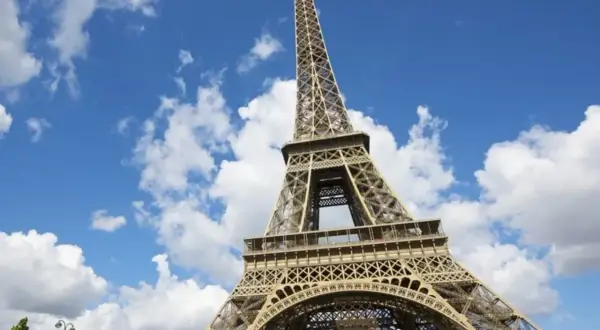 Vue en contre-plongée du برج ايفل sous un ciel bleu parsemé de nuages blancs.