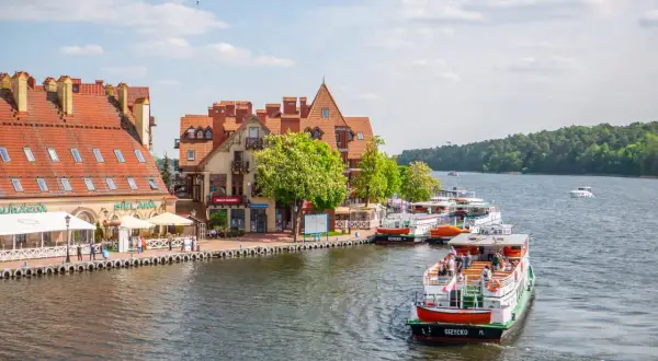 Port w Giżycku z cumującymi statkami i budynkami z czerwonymi dachami. Widać łodzie wycieczkowe, idealne na odkrywanie giżyckich atrakcji.