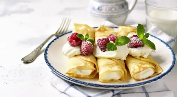 Rolowane naleśniki z mascarpone, ozdobione malinami i miętą, wyglądają apetycznie. Idealne na deser!
