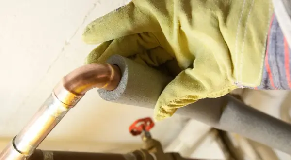 Hand mit Handschuh isoliert Kupferrohre, um Heizungsrohre zu verlegen und Energieverlust zu minimieren.