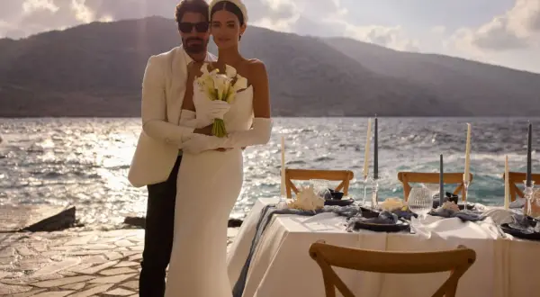 Un couple marié, maridat 19 63, pose près de la mer. La mariée tient un bouquet de callas. Une table de réception est dressée.